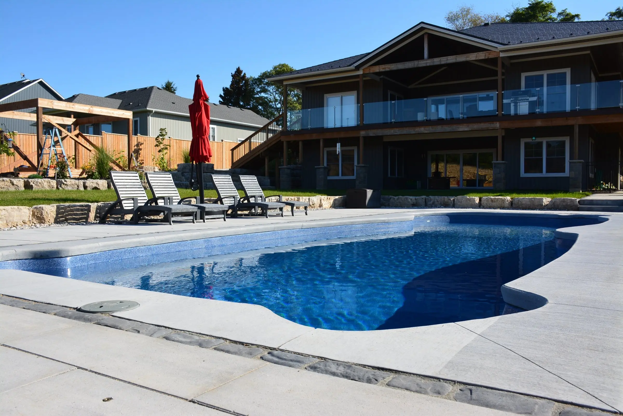 Kidney pool with lounge chairs below a walkout deck